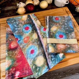 May include: Two tea towels with a colorful abstract design featuring circles and swirls in shades of red, blue, yellow, and green. The towels are made of 100% cotton and are packaged together. The text on the package reads "Samantha Hall Art 100% Cotton Tea Towel".