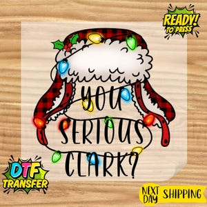 May include: A DTF transfer featuring a Santa hat with a red and black plaid pattern, adorned with colorful Christmas lights. The text "YOU SERIOUS CLARK?" is displayed in black, with "READY! TO PRESS" and "DTF TRANSFER" graphics.