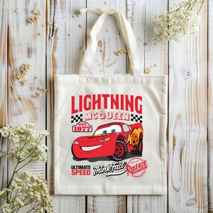 May include: Off-white canvas tote bag featuring a red Lightning McQueen race car graphic. The design includes the text "LIGHTNING MCQUEEN" in red, with "est. 1977" and "ULTIMATE SPEED Think Fast Rust-eze" also printed on the bag.