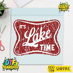 May include: A red and white DTF transfer with the text "IT'S Lake TIME" in a distressed style. The design is on a light blue background, with additional text indicating it is ready to press.