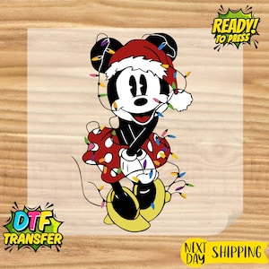 May include: A DTF transfer featuring a cartoon character wearing a Santa hat and a red dress with white polka dots, wrapped in colorful Christmas lights. The image includes the text "READY! TO PRESS" and "DTF TRANSFER".