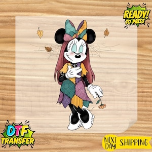 May include: A graphic illustration of a cartoon mouse character with long reddish-brown hair, wearing a patchwork dress and bow, featuring stitched facial details, holding a small orange flower, surrounded by spiderwebs and falling autumn leaves.