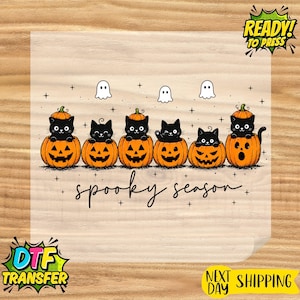 May include: A heat transfer design featuring six black cats sitting inside carved orange jack-o'-lantern pumpkins. Above the cats are three small white ghosts and small black crosses. The text "spooky season" is written in black cursive script.