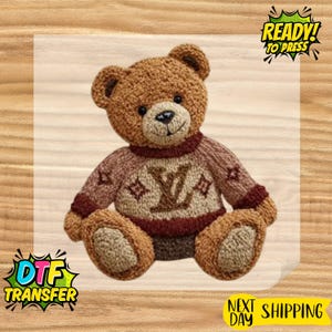 May include: A brown teddy bear wearing a sweater with a logo design. The bear has a stitched nose and mouth, and the text "READY! TO PRESS" is visible. The image also includes the text "DTF TRANSFER".