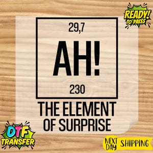 May include: A DTF transfer sheet with the text "AH!" in large, bold, black letters, with the numbers 29,7 and 230 above and below. The phrase "THE ELEMENT OF SURPRISE" is below the text. The sheet also has "READY! TO PRESS" and "NEXT DAY SHIPPING" graphics.