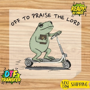 May include: A light green frog riding a white scooter, holding a brown book with a cross. The text "OFF TO PRAISE THE LORD" is arched above the frog. The image also includes "READY! TO PRESS" and "DTF TRANSFER".