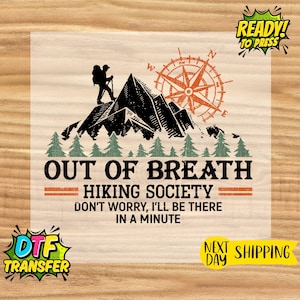 May include: A DTF transfer featuring a mountain scene with a hiker, compass, and text that reads "OUT OF BREATH HIKING SOCIETY." The design includes pine trees and the phrase "DON'T WORRY, I'LL BE THERE IN A MINUTE."