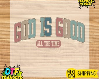 May include: A ready-to-press DTF transfer with the text "GOD IS GOOD ALL THE TIME" in a retro font. The text is in shades of pink, blue, and gray. The transfer is on a light background.
