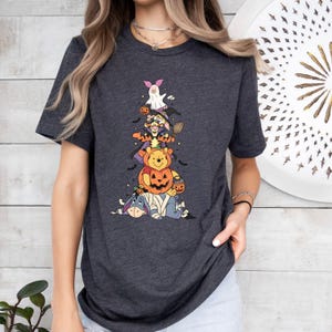 Op de afbeelding: Een donkergrijs gem&ecirc;leerd T-shirt met korte mouwen en een verticale stapel stripfiguren in Halloween-kostuums, waaronder Knorretje als spook, Teigetje als heks, Winnie de Poeh in een pompoen en Iejoor als mummie.