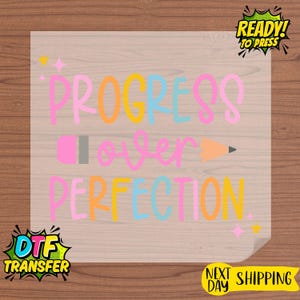 May include: A transparent DTF transfer with the text "PROGRESS OVER PERFECTION" in pink, orange, yellow, and blue. A pink pencil and orange pencil are also featured. The transfer is ready to press.