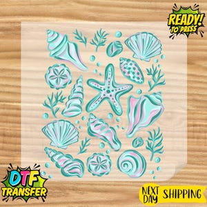 May include: A DTF transfer sheet featuring a collection of various seashells, starfish, and coral branches in shades of teal, light blue, and soft pink. The design includes scattered small bubbles and the text READY TO PRESS and DTF TRANSFER.