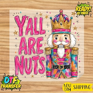 May include: A colorful nutcracker illustration featuring a gold crown, white beard, and a vibrant uniform with pink, blue, and orange accents. The text Y'ALL ARE NUTS is written in large pink letters to the left. Includes small gold star accents.