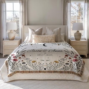 May include: A cream-colored throw blanket with a floral design and the names "Jason & Anna" and the date "09-07-2025" printed on it. The blanket has a fringe border and is decorated with flowers in red, yellow, and black.