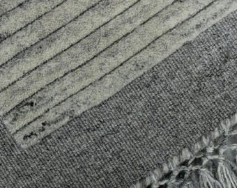May include: Close-up of a grey and white rug with a striped pattern. The rug has a textured surface with a fringe detail on the bottom right corner. The design features alternating stripes of light grey and darker grey.