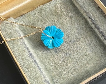 Op de afbeelding: Een turquoise bloemenhangerketting met een gouden ketting. De hanger zit in een doos met een lichtbruine fluwelen voering.