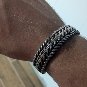 May include: A braided bracelet with a mix of silver and copper-colored metal. The bracelet is thick and has a textured, woven appearance. The design features a combination of dark silver and copper tones.
