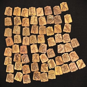 May include: A collection of over 50 small, antique, brass-colored metal tokens. Each token features a different design, including sports, animals, and abstract patterns. The tokens are arranged in a grid pattern on a black surface.