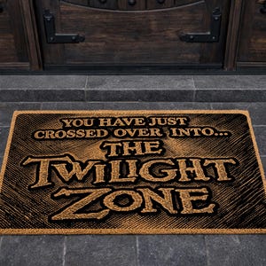 May include: A rectangular doormat with the text "YOU HAVE JUST CROSSED OVER INTO... THE TWILIGHT ZONE" in a vintage style. The mat is brown with black text and sits in front of a dark wooden door.