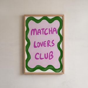 May include: A rectangular wall art print in a light wooden frame featuring a pale pink background with a wavy dark green border. The text MATCHA LOVERS CLUB is printed in the centre in a bold, hand-lettered style using a vibrant purple colour.