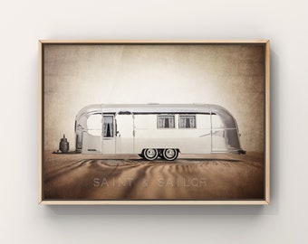 May include: A vintage silver Airstream trailer parked on a brown dirt road with the text "SAINT & SAILOR" printed below.