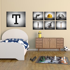 May include: A child's bedroom with a white bed, a wooden dresser, and a board game on the floor. The wall features a large black and white letter "T" and six framed images of construction tools, including a drill and a hammer.