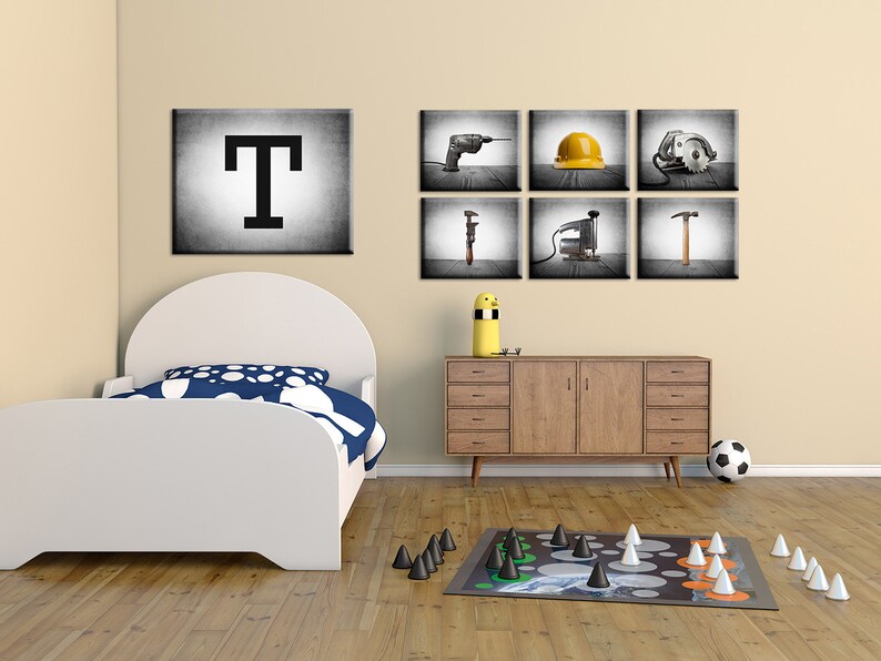May include: A child's bedroom with a white bed, a wooden dresser, and a board game on the floor. The wall features a large black and white letter "T" and six framed images of construction tools, including a drill and a hammer.