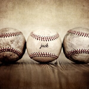 May include: Three vintage baseballs, one with the word "jack" written on it, are lined up on a wooden surface. The baseballs are worn and have a faded, vintage look.