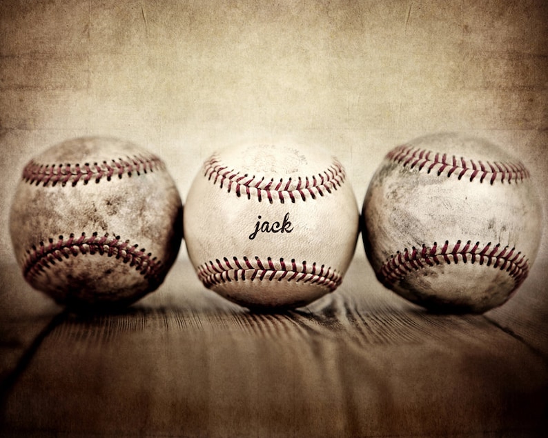 May include: Three vintage baseballs, one with the word "jack" written on it, are lined up on a wooden surface. The baseballs are worn and have a faded, vintage look.