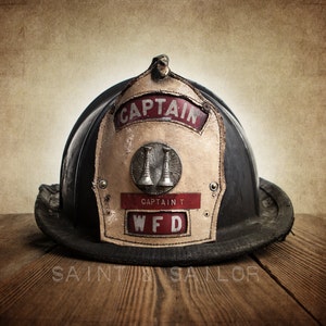 May include: A vintage black leather firefighter helmet with a brass bell and a white leather patch that reads "Captain WFD".