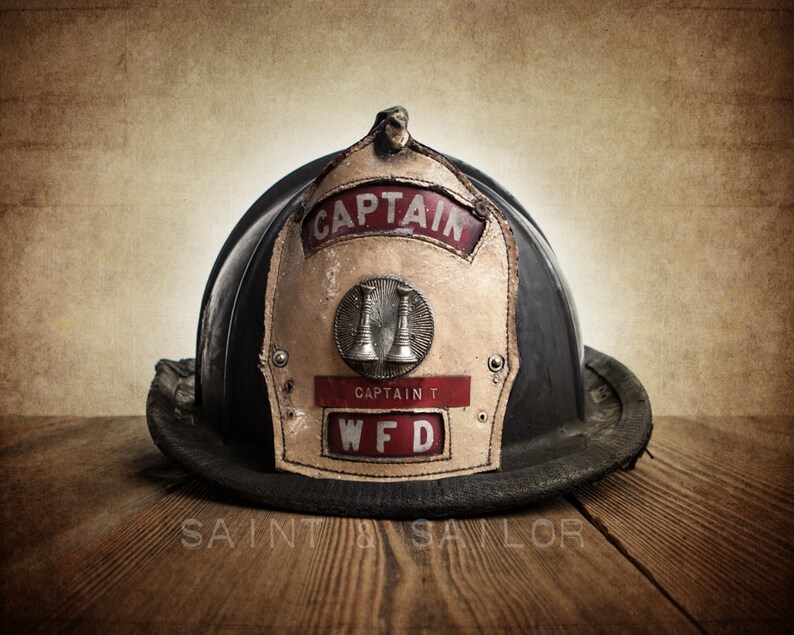 May include: A vintage black leather firefighter helmet with a brass bell and a white leather patch that reads "Captain WFD".