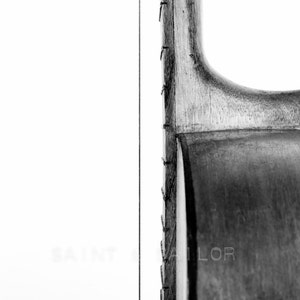 May include: Close-up of the side of an acoustic guitar, showing the wood grain and the strings. The guitar is black and has a natural wood finish.