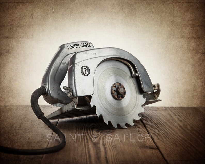 May include: Vintage Porter-Cable circular saw with a silver metal housing and a large, circular blade. The saw has a black power cord and is resting on a wooden surface. The number "6" is visible on the side of the saw.
