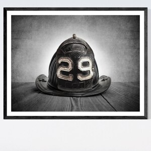 May include: A black leather firefighter helmet with the number "29" on the front, sitting on a wooden surface.