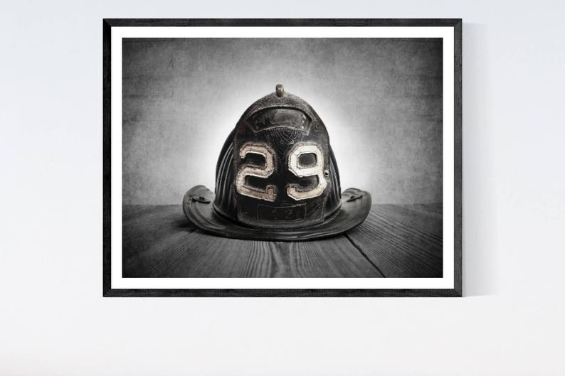 May include: A black leather firefighter helmet with the number "29" on the front, sitting on a wooden surface.