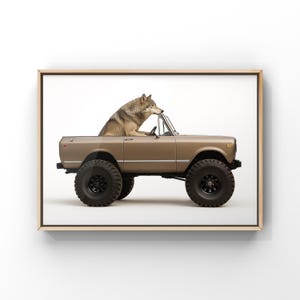 May include: A framed print featuring a brown vintage SUV with large black tires. A gray wolf is sitting in the driver's seat, resting its paws on the steering wheel. The artwork is set against a white background.