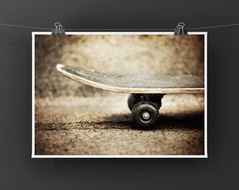 May include: A close-up shot of a skateboard on a textured surface. The skateboard has a black deck with visible wear and tear, and black wheels. The image has a vintage, slightly faded aesthetic.