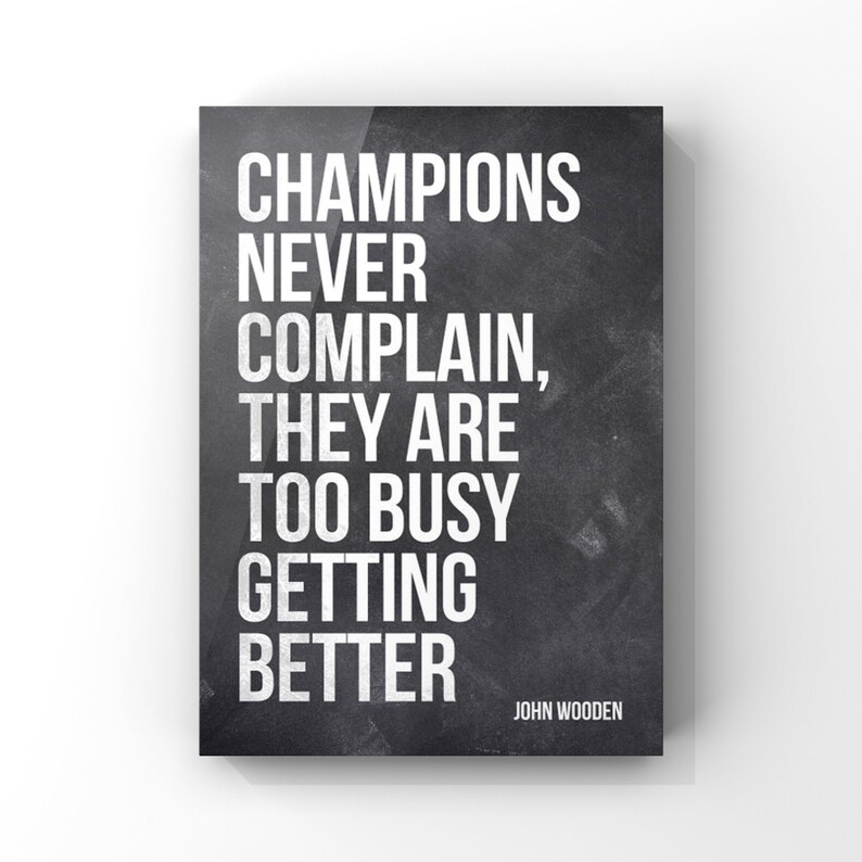 May include: Black and white motivational quote on a chalkboard background. The quote reads "Champions never complain, they are too busy getting better." The quote is attributed to John Wooden.