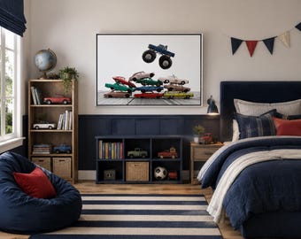 Puede incluir: Una impresión artística enmarcada que muestra una pila de coches de juguete coloridos con un camión monstruo azul saltando sobre ellos. La obra se exhibe en un dormitorio con una cama azul marino, una alfombra a rayas, una estantería de madera y un mueble.