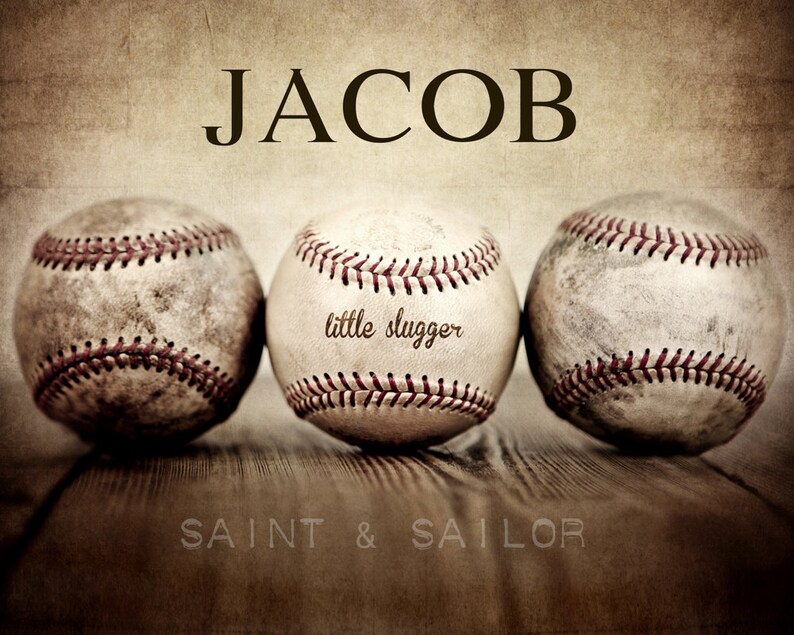 May include: Three vintage baseballs with red stitching on a wooden surface. The middle baseball has the text "little slugger" written on it. The text "JACOB" is at the top of the image and the text "SAINT & SAILOR" is at the bottom of the image.