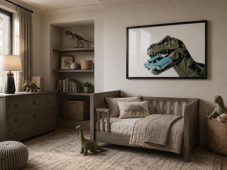 Op de afbeelding: Een ingelijste kunstdruk met een groene Tyrannosaurus Rex die in een lichtblauwe vintage auto bijt. Het kunstwerk hangt in een kamer met een houten peuterbed, een dressoir, planken met dinosaurusdecoratie en een getextureerd vloerkleed.