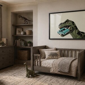 Op de afbeelding: Een ingelijste muurkunstprint met een groene Tyrannosaurus Rex die een kleine turquoise speelgoedauto in zijn bek houdt. Het kunstwerk hangt in een kamer met een houten peuterbed, een dressoir, planken met dinosaurusdecor en een vloerkleed.