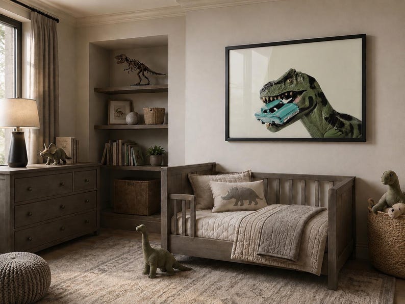 Op de afbeelding: Een ingelijste muurkunstprint met een groene Tyrannosaurus Rex die een kleine turquoise speelgoedauto in zijn bek houdt. Het kunstwerk hangt in een kamer met een houten peuterbed, een dressoir, planken met dinosaurusdecor en een vloerkleed.