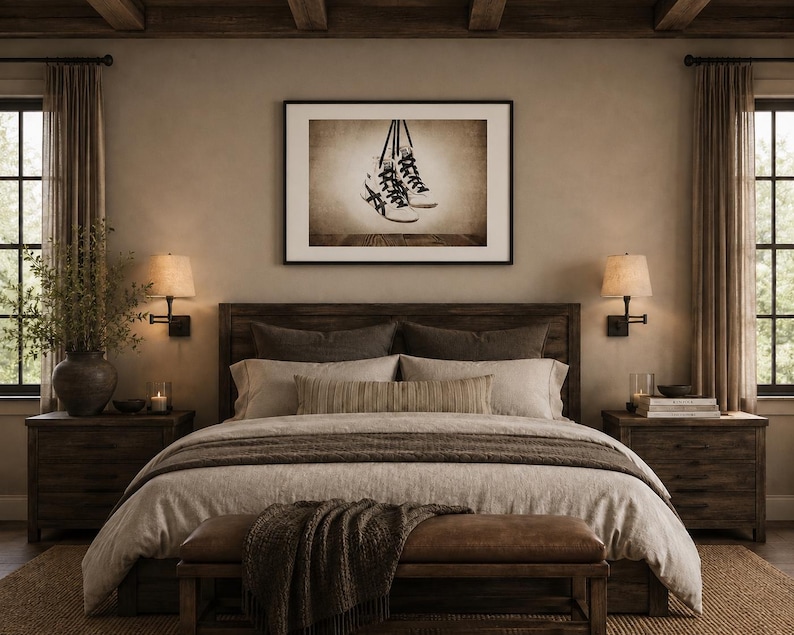 May include: A framed wall art print featuring a sepia-toned illustration of a pair of high-top sneakers with black laces hanging by their laces. The artwork is displayed in a simple black frame and is centered above a wooden bed frame in a bedroom.