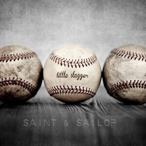 May include: Three vintage baseballs with red stitching, one with the text "little slugger" on it, on a wooden surface with the text "SAINT & SAILOR" below.