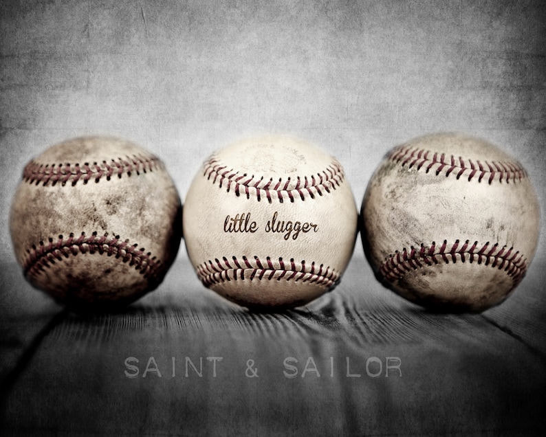 May include: Three vintage baseballs with red stitching, one with the text "little slugger" on it, on a wooden surface with the text "SAINT & SAILOR" below.