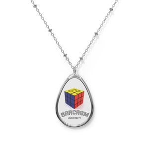 May include: Silver-toned necklace with a teardrop pendant. The pendant features a Rubik's Cube design in yellow, blue, and red, with the words "SARCASM UNIVERSITY" in black. The chain is a delicate link style.