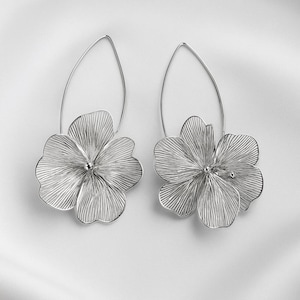 K&ouml;nnte beinhalten: Ein Paar silberfarbene Blumenohrringe. Jeder Ohrring hat ein detailliertes, durchbrochenes Blumendesign, das an einem tropfenf&ouml;rmigen Draht h&auml;ngt. Die Blumen haben ein strukturiertes, geripptes Aussehen mit einer kleinen Perle in der Mitte.