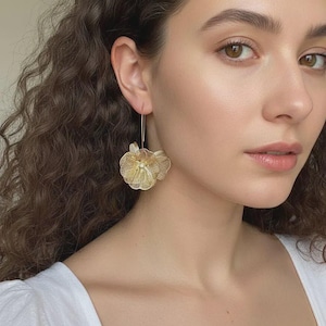 K&ouml;nnte beinhalten: Goldfarbene Blumenohrringe. Die Ohrringe haben ein zartes, durchbrochenes Design, das einer Blume &auml;hnelt. Die Ohrringe sind an einem d&uuml;nnen, goldfarbenen Draht aufgeh&auml;ngt. Die Ohrringe sind ein Statement-St&uuml;ck und verleihen einen Hauch von Eleganz.