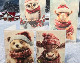 May include: Four Christmas cards with watercolour illustrations of animals in winter clothing. The cards show an owl, camel, bear, and cow, each wearing a Santa hat and scarf. The background depicts a snowy landscape with mountains and houses.