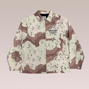 Puede incluir: Chaqueta de camuflaje en tonos beige, marr&oacute;n y negro, con el texto azul marino "GALLERY DEPT" en el pecho. La chaqueta tiene cuello, cremallera y dos bolsillos delanteros. La chaqueta es de color neutro y apta para cualquiera.